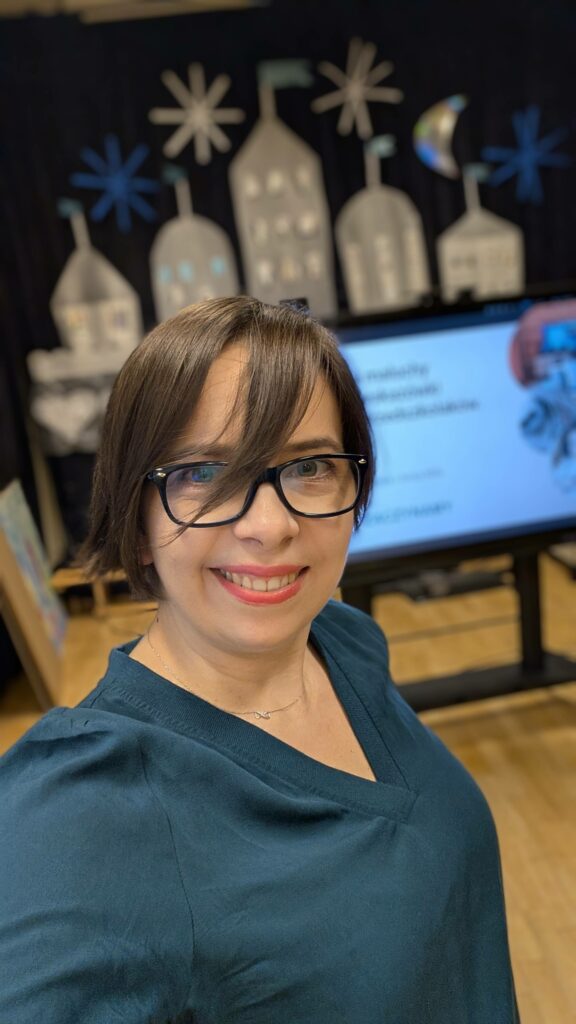 uśmiechnięta w okularach kobieta na tle tablicy multimedialnej