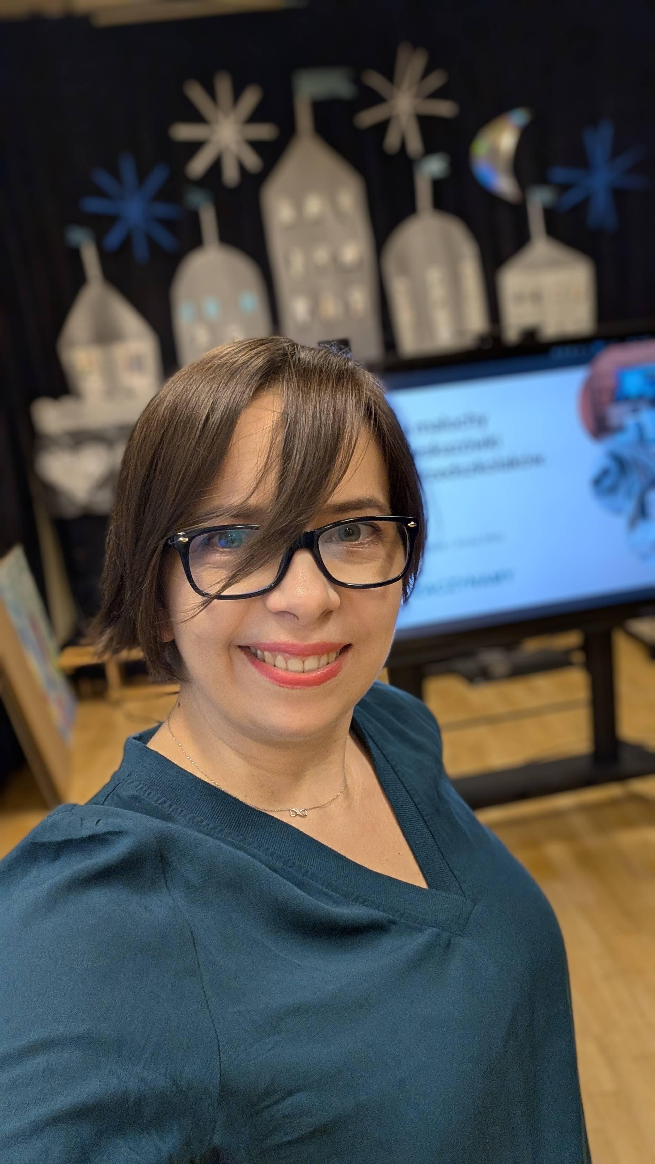 uśmiechnięta w okularach kobieta na tle tablicy multimedialnej