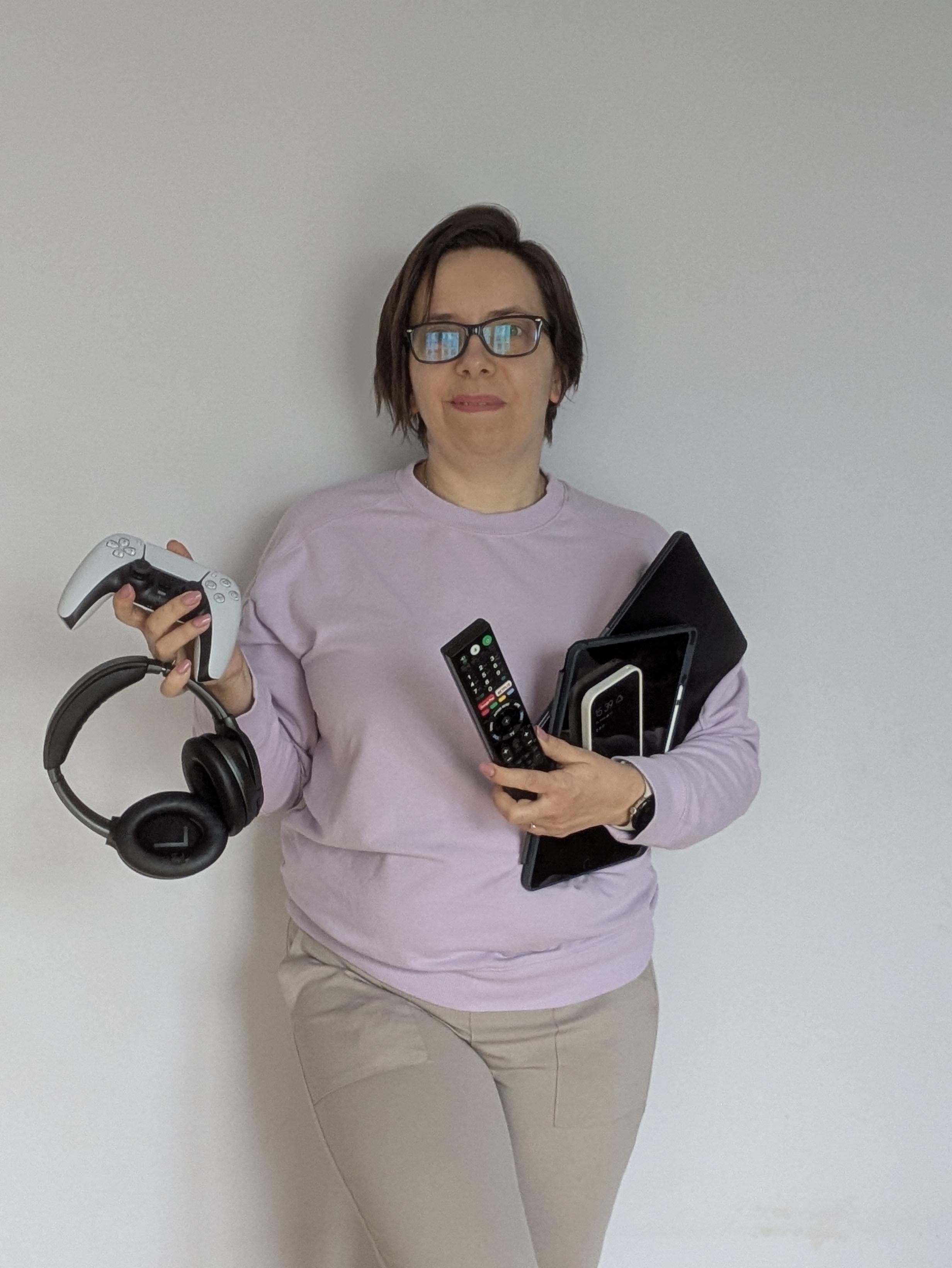 Beata Broniek trzyma wiele urzadzeń cyfrowych - m.in. tablet, smartfon, słuchawki, laptopa, pad od konsoli. Ma to pokazać wielość urządzeń jaką obecnie zarządzają rodzice.